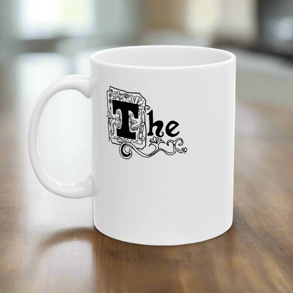 A white ceramic mug with a black printed text design that includes the word 'The' in an abstract art style.