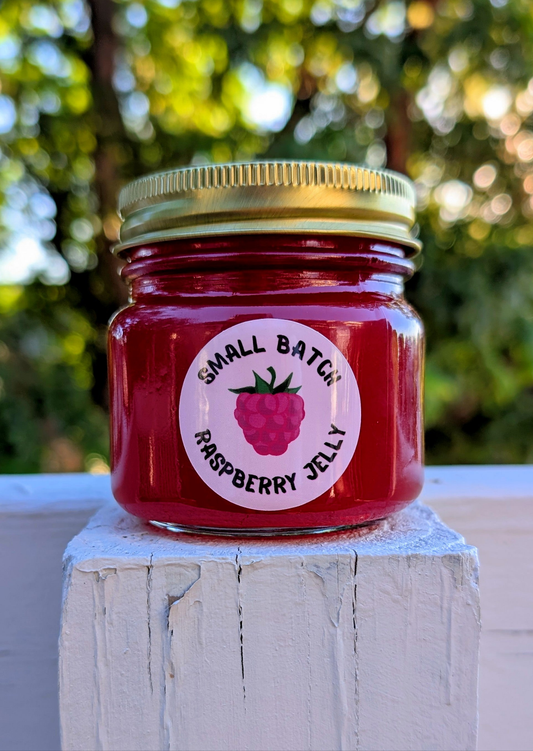 small batch NEEDMOREJELLY raspberry jelly in an 8oz jar with a golden twist on lid and a circle shaped raspberry labels designed by JellyfishParty