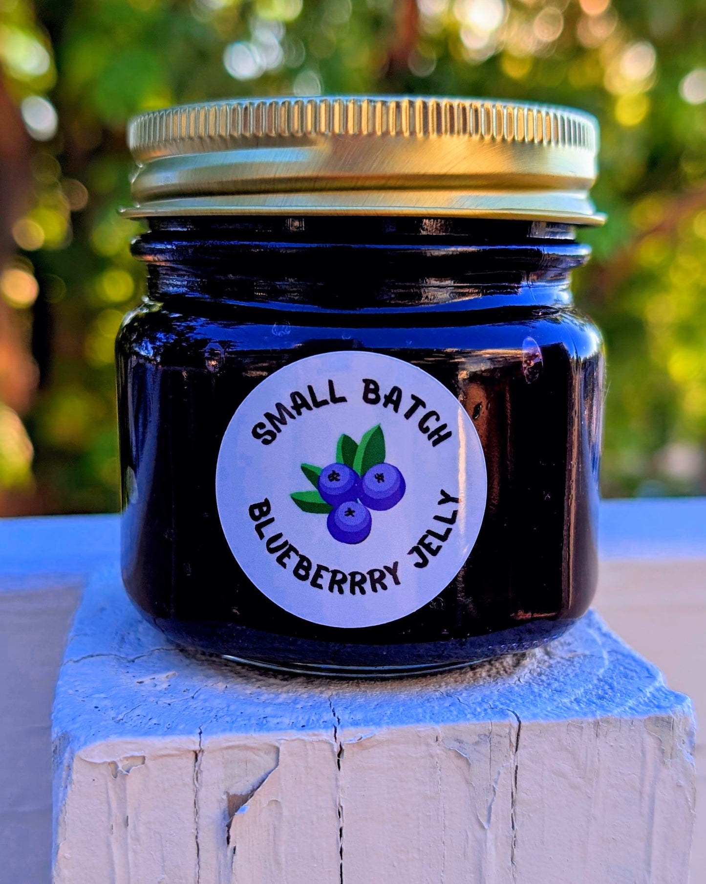 Jar of small batch blueberry jelly with a label on a wooden block against a blurred green background made by JellyfishParty