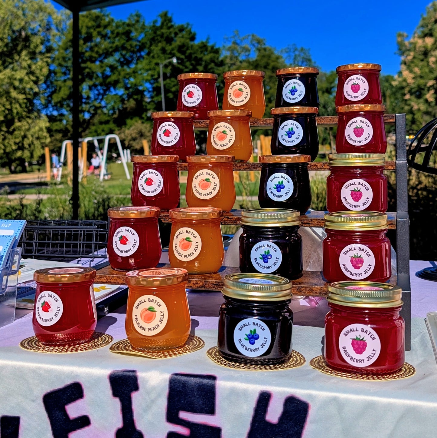 four tiers of vibrant jelly lined up outside on a table with the following flavors: strawberry, palisade peach, blueberrry and raspberry.