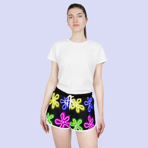 white female model wearing womens shorts that are black with neon flower clouds displayed across the entire pattern. has white drawstrings and trim.