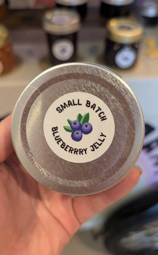 Small batch blueberry jelly jar lid held by a hand with blurred jars in the background.