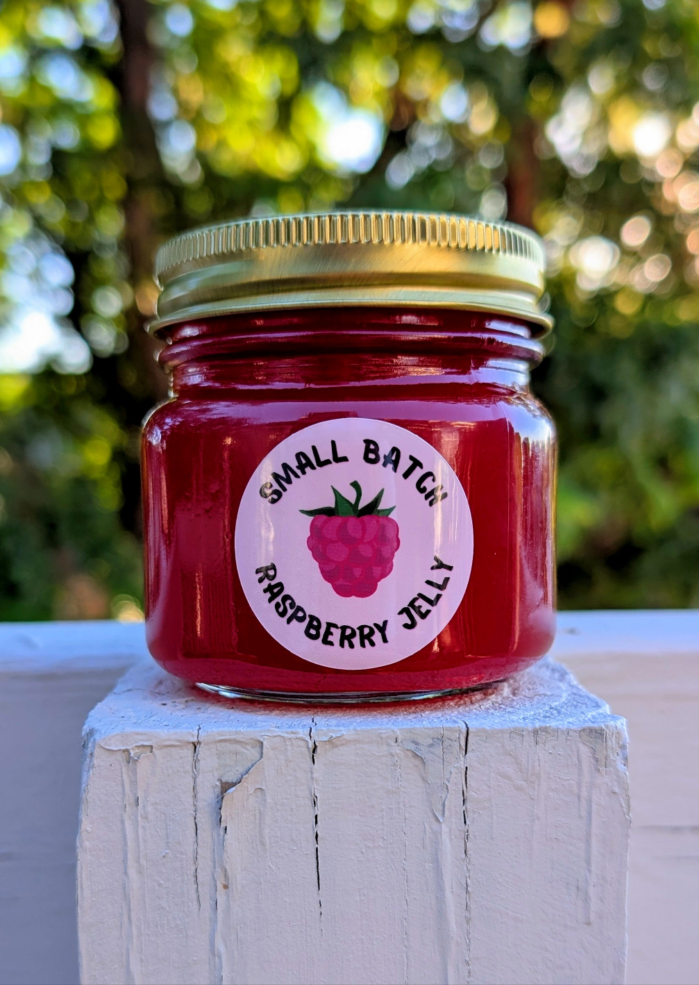small batch NEEDMOREJELLY raspberry jelly in an 8oz jar with a golden twist on lid and a circle shaped raspberry labels designed by JellyfishParty 