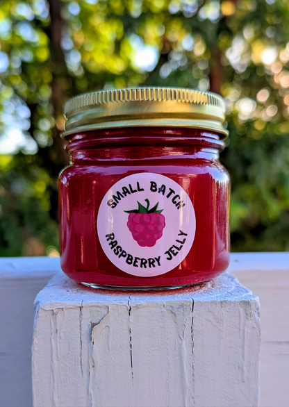 small batch NEEDMOREJELLY raspberry jelly in an 8oz jar with a golden twist on lid and a circle shaped raspberry labels designed by JellyfishParty 