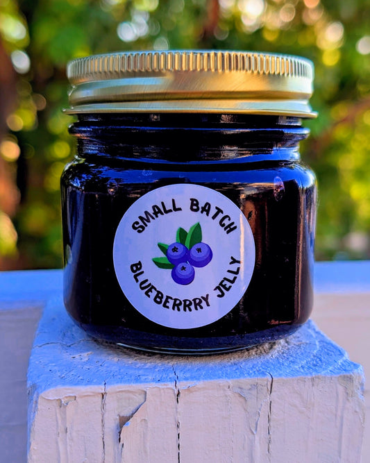 Jar of small batch blueberry jelly with a label on a wooden block against a blurred green background made by JellyfishParty