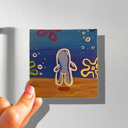 colorful magnet depicting a painting of a bubble shaped person floating underwater with flower clouds and tiny bubbles in the background, the magnet is held up in front of a magnetic refrigerator background
