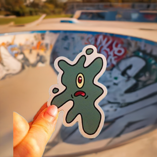 green squished magnet held up in front of a skate park bowl with graffiti